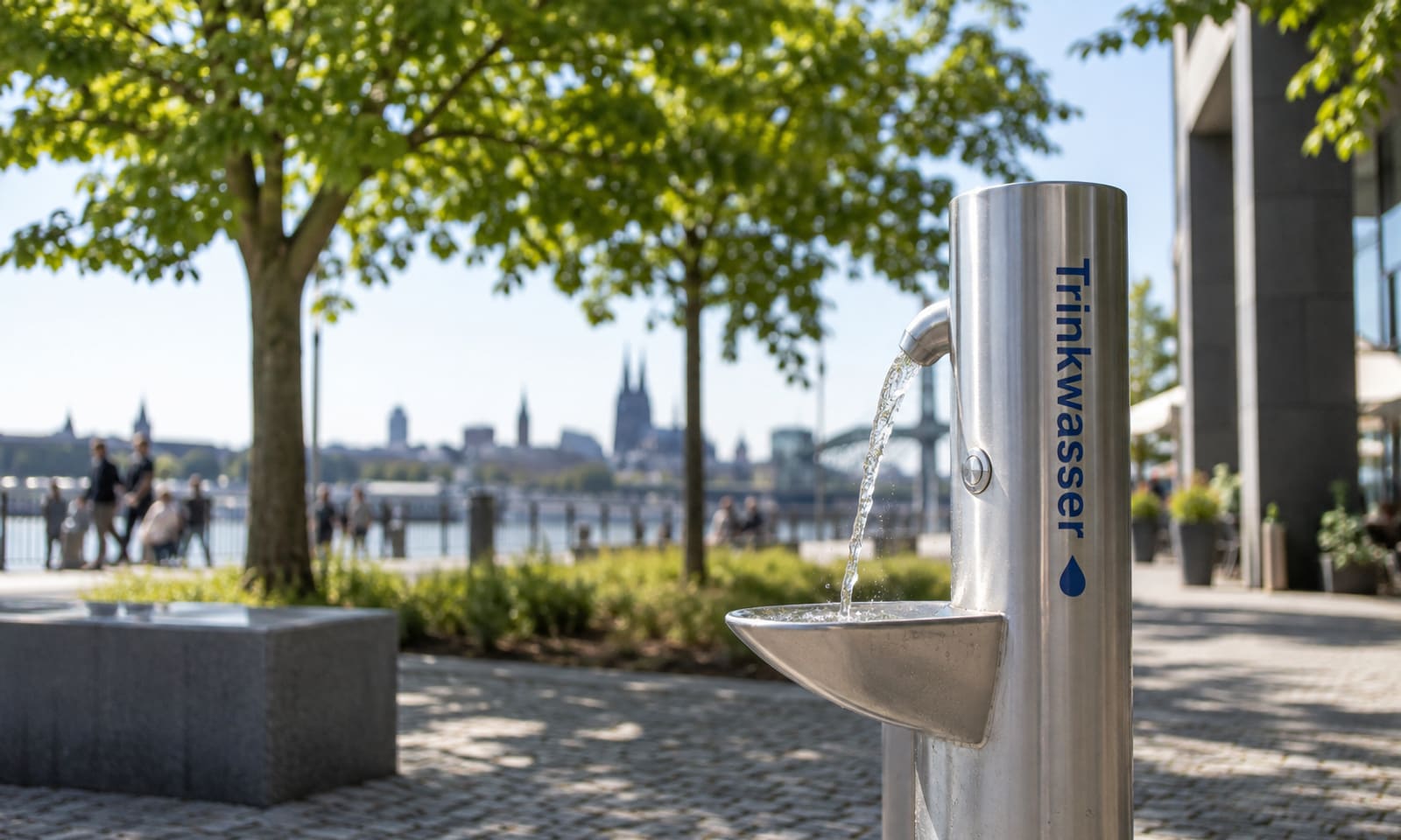 Edelstahl-Trinkbrunnen mit der Aufschrift Trinkwasser und laufendem Wasserstrahl in einer Parkanlage am Fluss